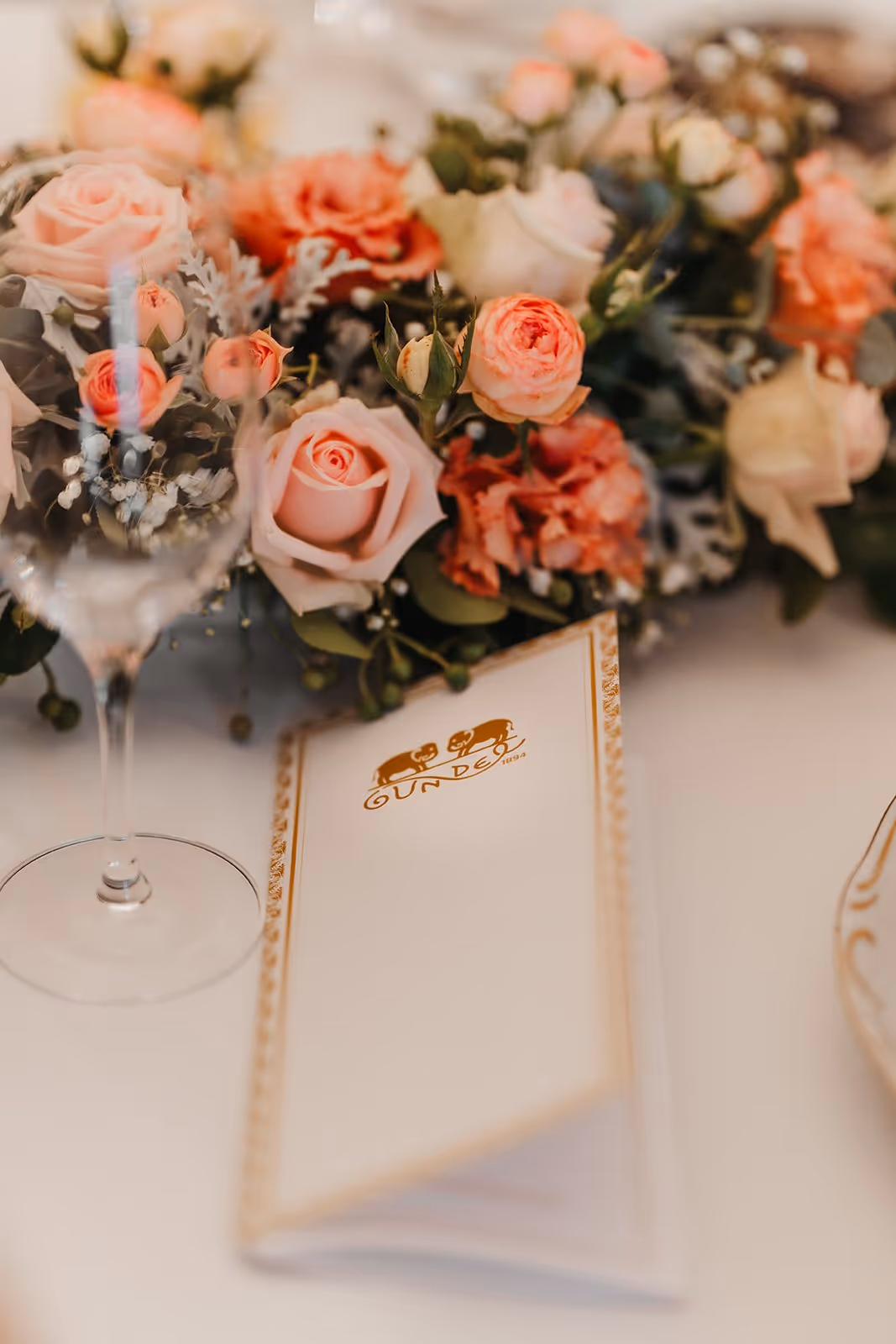 Elegant table setting with pink roses, a wine glass, and a folded menu featuring a gold logo and border.