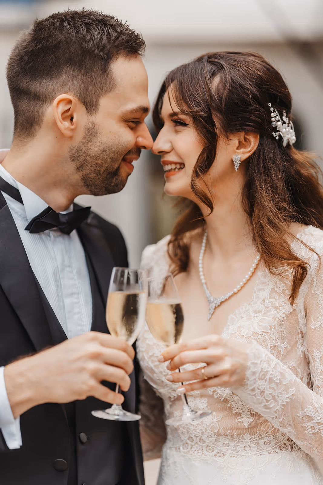 Bride and groom smiling and clinking champagne glasses while leaning their noses together.