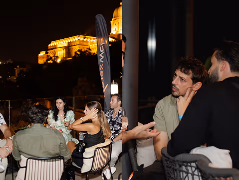 Group of people engaged in conversation while seated outdoors at night with a lit historic building in the background.