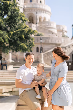 Smiling family of three with a toddler posing outdoors near historic stone architecture and stairs.