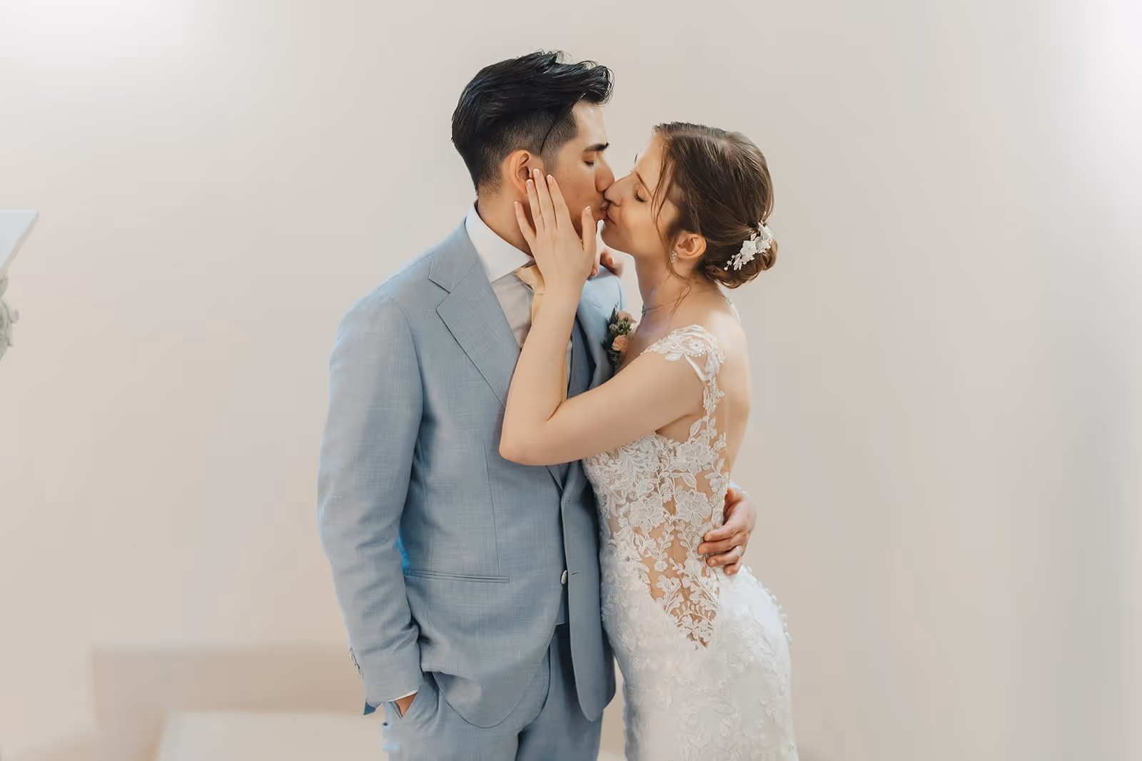 Bride and groom sharing a kiss, with the bride in a lace wedding dress and the groom in a light blue suit.