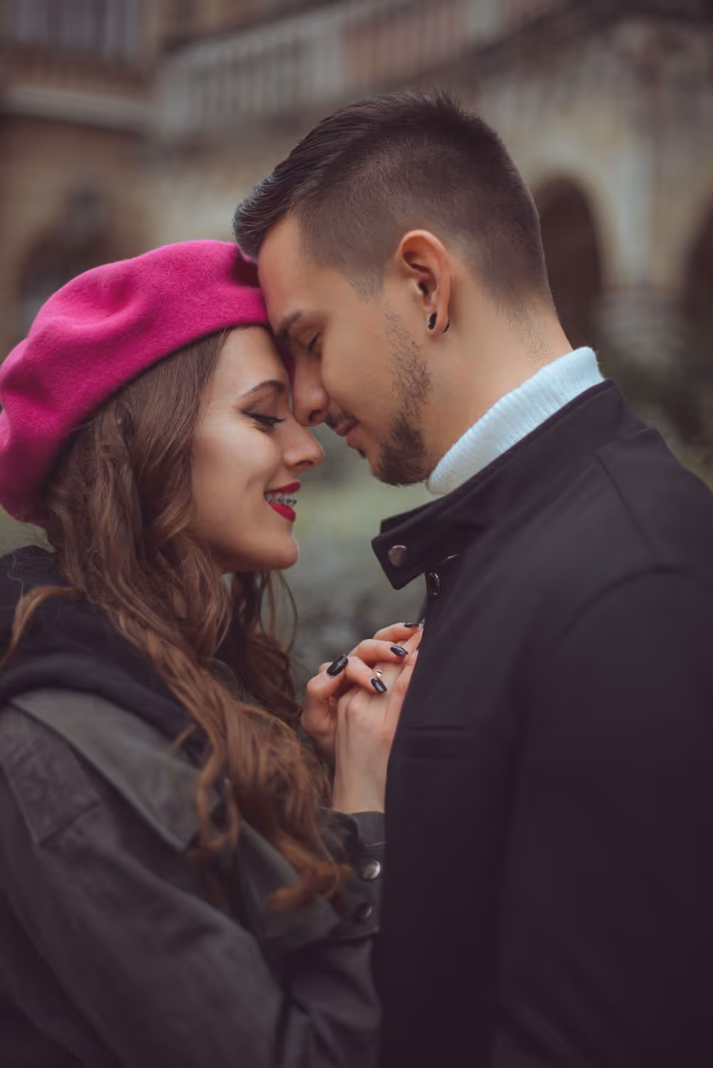 Couple touching foreheads affectionately while holding hands outdoors.