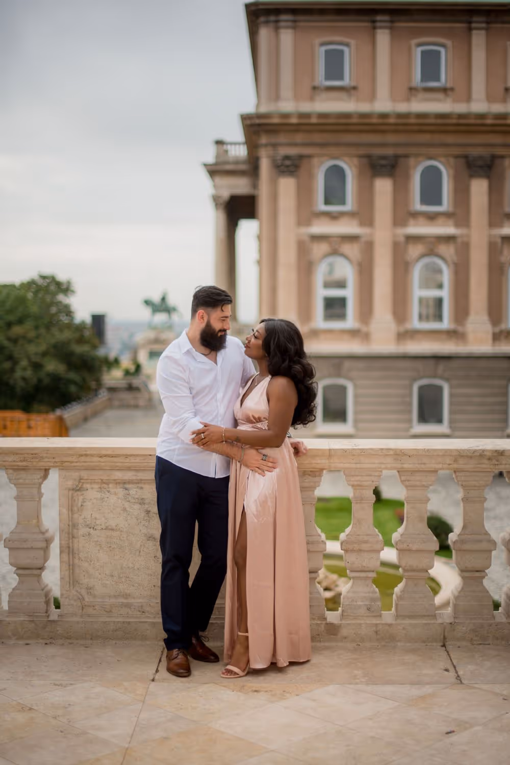 Couple embracing on a balcony with a historic building in the background.