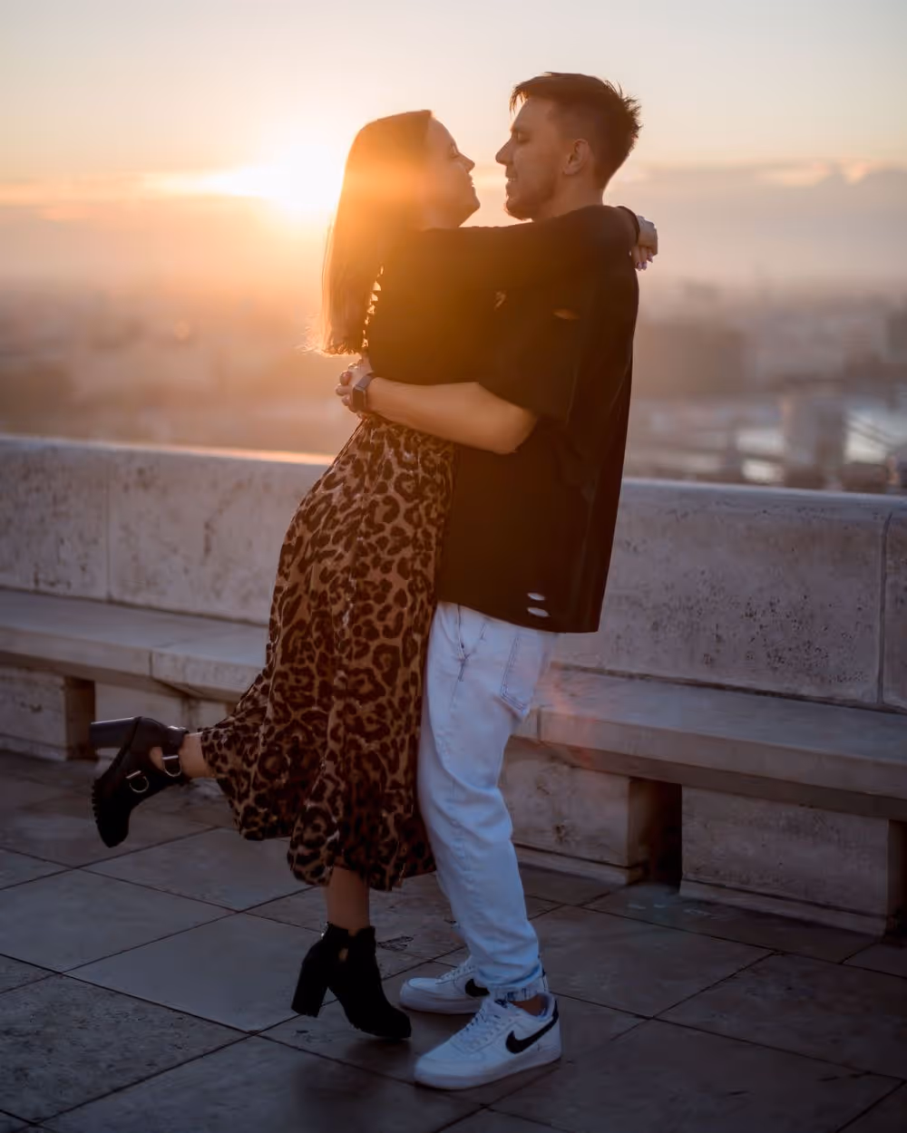 Couple embracing outdoors at sunset, with cityscape blurred in the background.