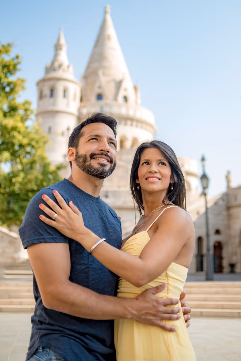 Smiling couple embracing outdoors with historic castle towers and clear blue sky in the background.