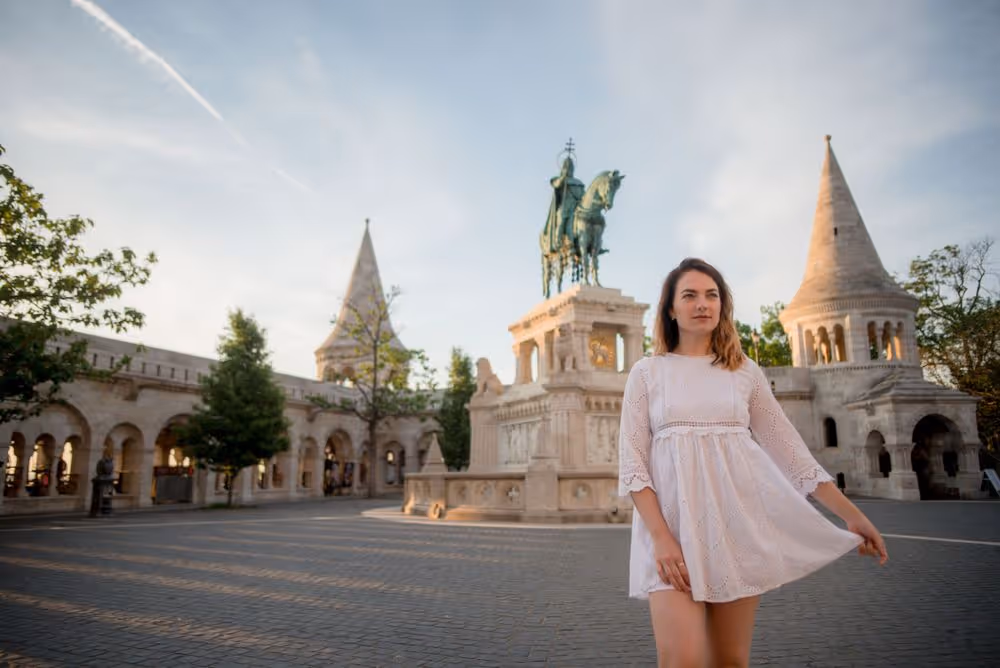 Woman in a white dress standing near the Fisherman's Bastion with a statue of St. Stephen on horseback in Budapest.