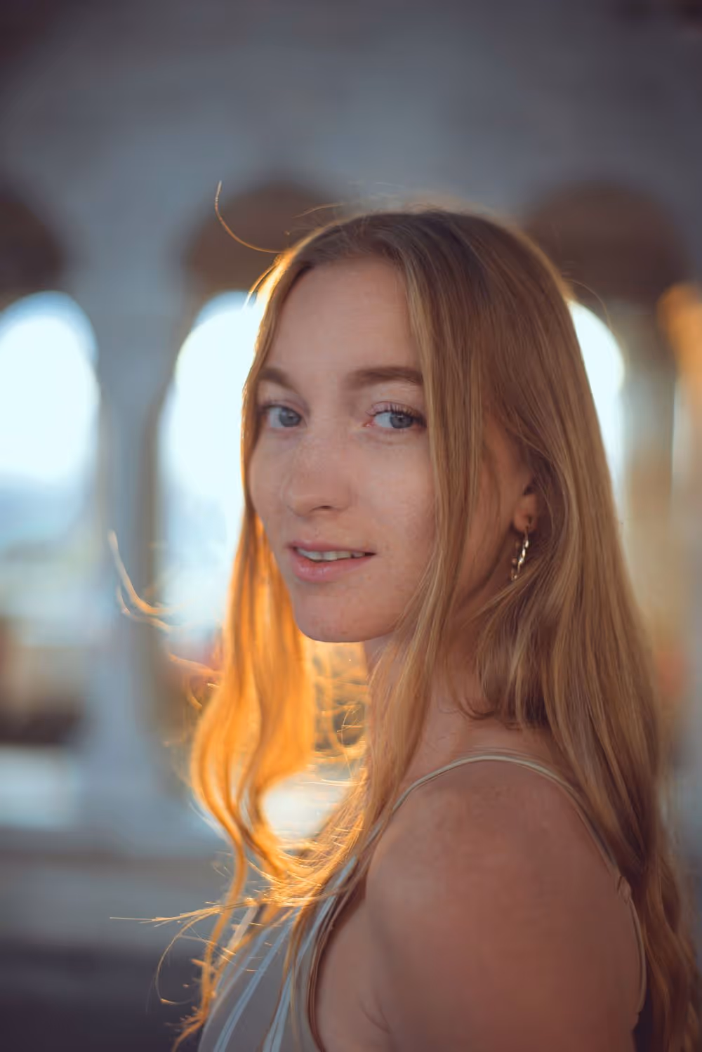 Young woman with long blonde hair looking over her shoulder with sunlit background arches.