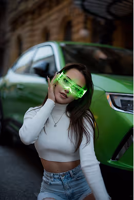 Young woman wearing futuristic green LED glasses posing in front of a green car on a street.