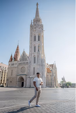 Man walking in front of a large historic white Gothic-style cathedral with a tall spire under clear blue sky.