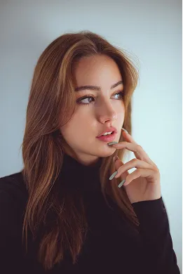 Young woman with long brown hair looking thoughtfully to the side, wearing a black turtleneck.
