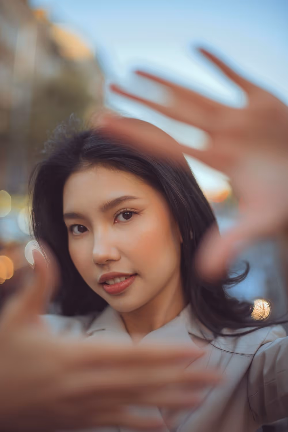 Close-up of a woman framing her face with her hands outdoors during sunset.