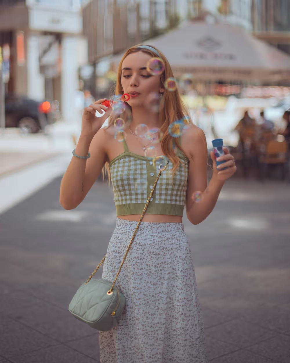 Young woman with long hair blowing soap bubbles on a city street.