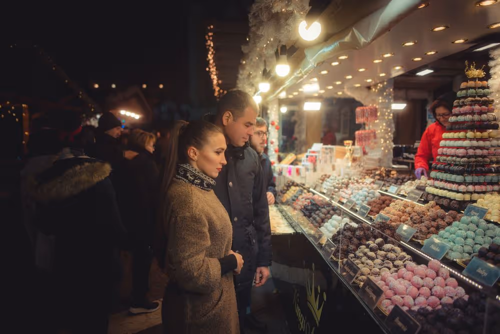 People browsing and selecting colorful confections displayed in glass cases at a well-lit outdoor market stall at night.